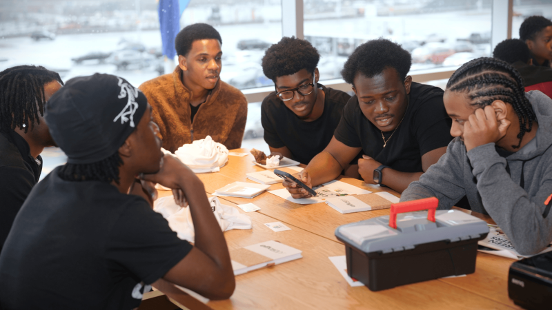 Group of young black men dressed in t-shirts, sitting at a table, having a discussion