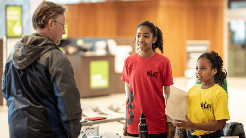 Two young girls dressed in red and yellow teachers speaking to an adult about business.